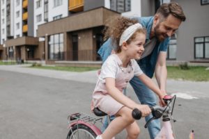 dziewczynka ucząca się jeździć na rowerze podtrzymywana przez tatę