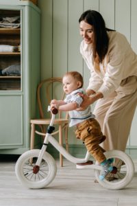 mama ucząca dziecko jazdy na biegowym rowerku dziecięcym