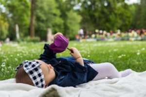 niemowlę z fioletowym kwiatem w ręku leży na białym kocu piknikowym